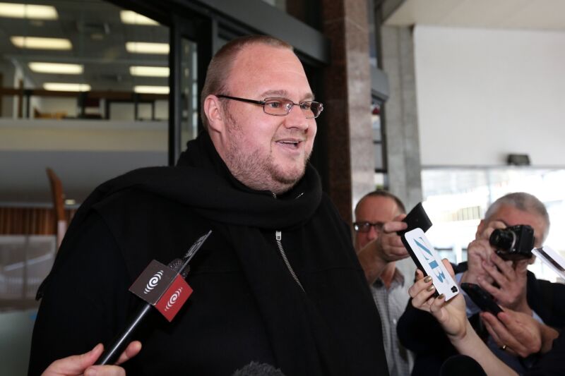 Kim Dotcom smiling and speaking to reporters outside a courthouse